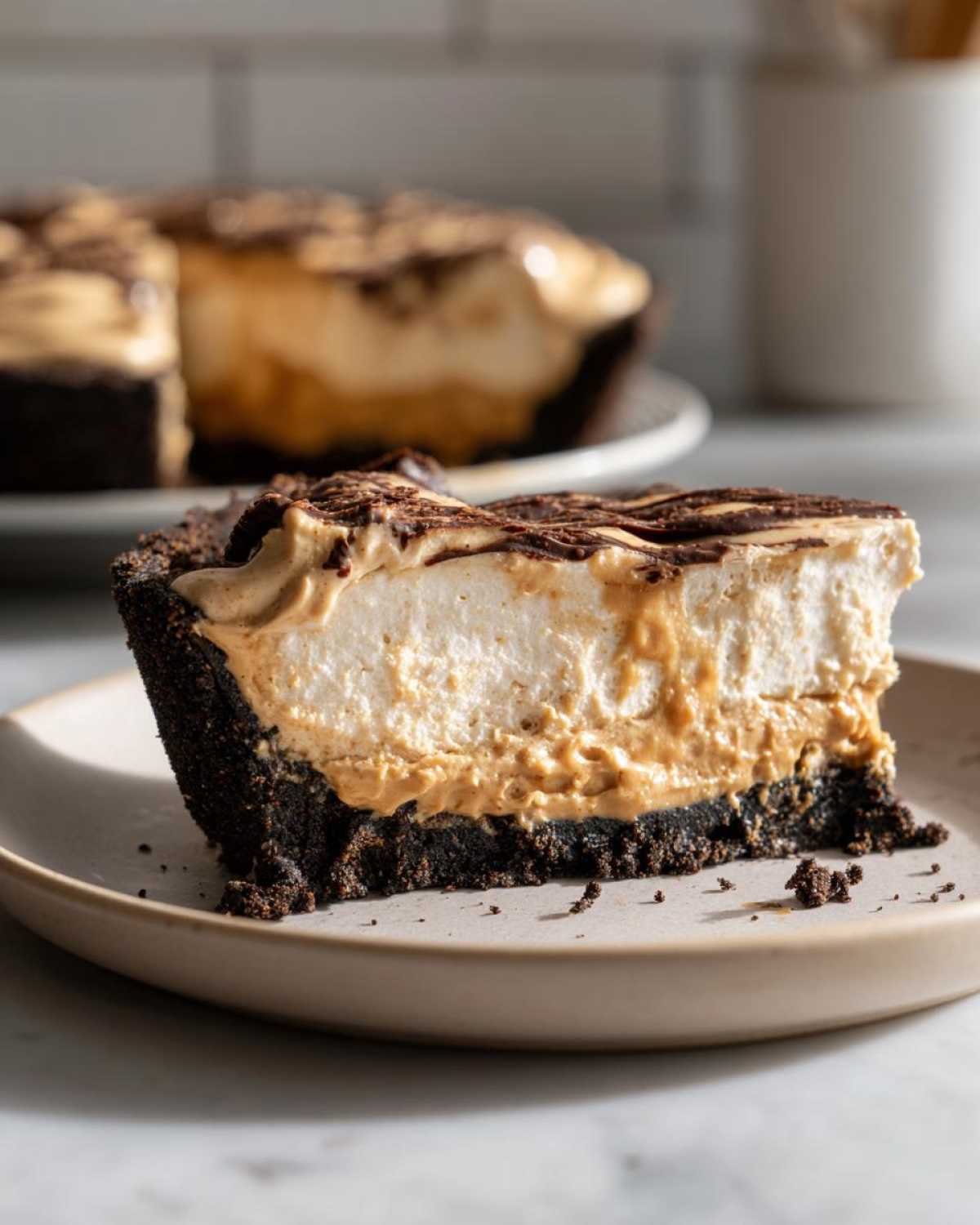 A close-up slice of rich peanut butter pie featuring a thick chocolate crust, creamy filling, and chocolate drizzle.