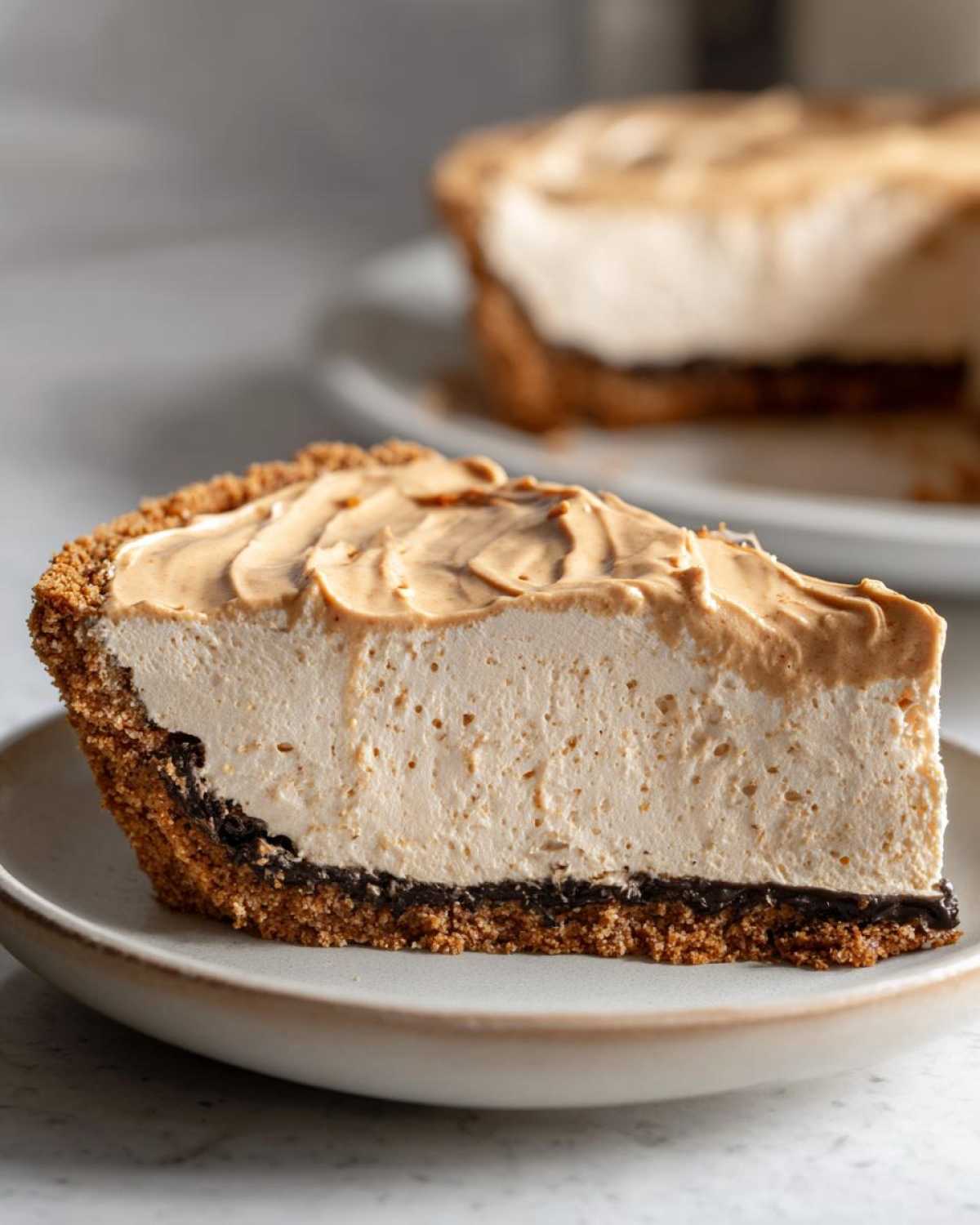 A thick slice of creamy peanut butter pie showing the graham cracker crust, chocolate layer, and peanut butter filling.