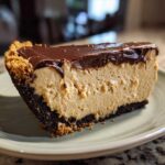 A thick slice of creamy peanut butter pie with a dark chocolate crust and rich chocolate ganache topping.