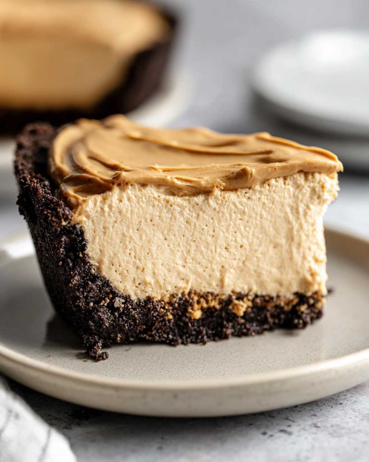 A thick slice of creamy peanut butter pie with a dark chocolate crust, topped with swirled peanut butter.