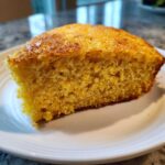 Close-up of a moist, golden slice of skillet cornbread served on a white plate.