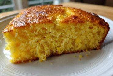 Close-up of a thick, moist slice of yellow skillet cornbread showing its crumb texture on a white plate.