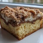 Close-up of a moist slice of sour cream coffee cake showing the crumb, cinnamon swirl, and thick streusel topping.
