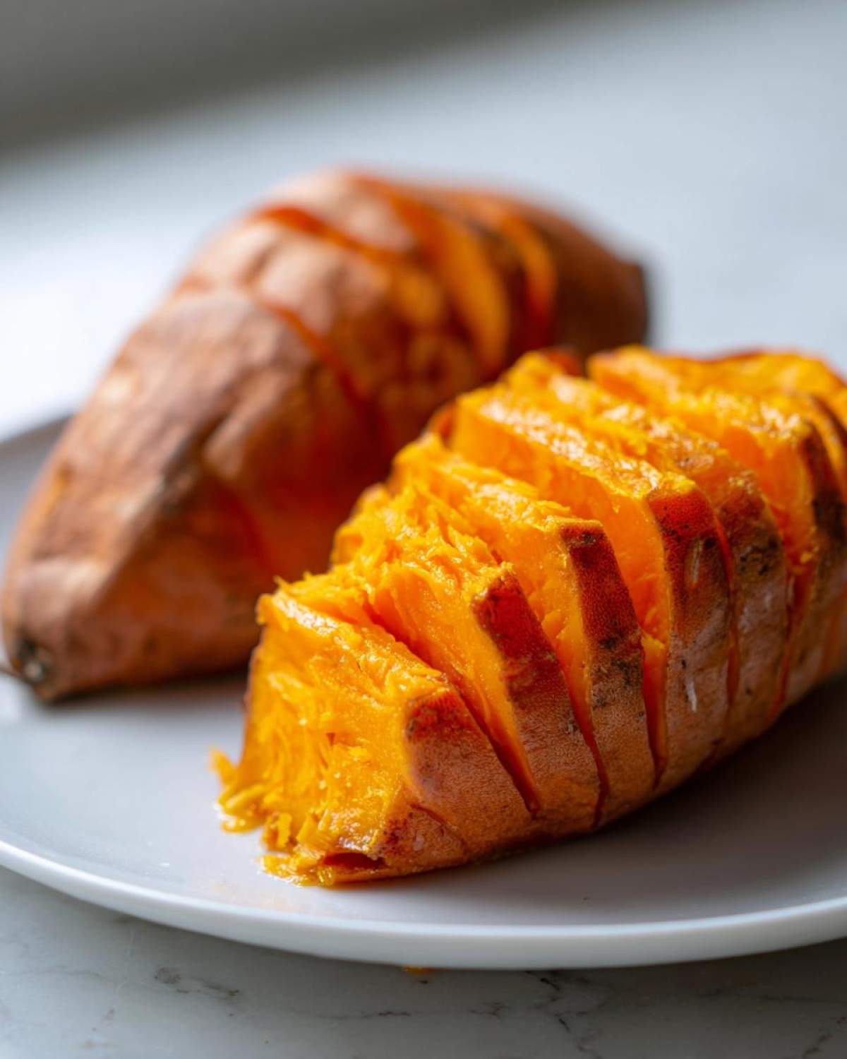 Close-up of two baked sweet potatoes, one sliced open to show the bright orange, fluffy interior.