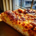 A close-up shot showing the thick, airy crumb and blistered, cheesy top of a slice made from sourdough discard pizza dough.