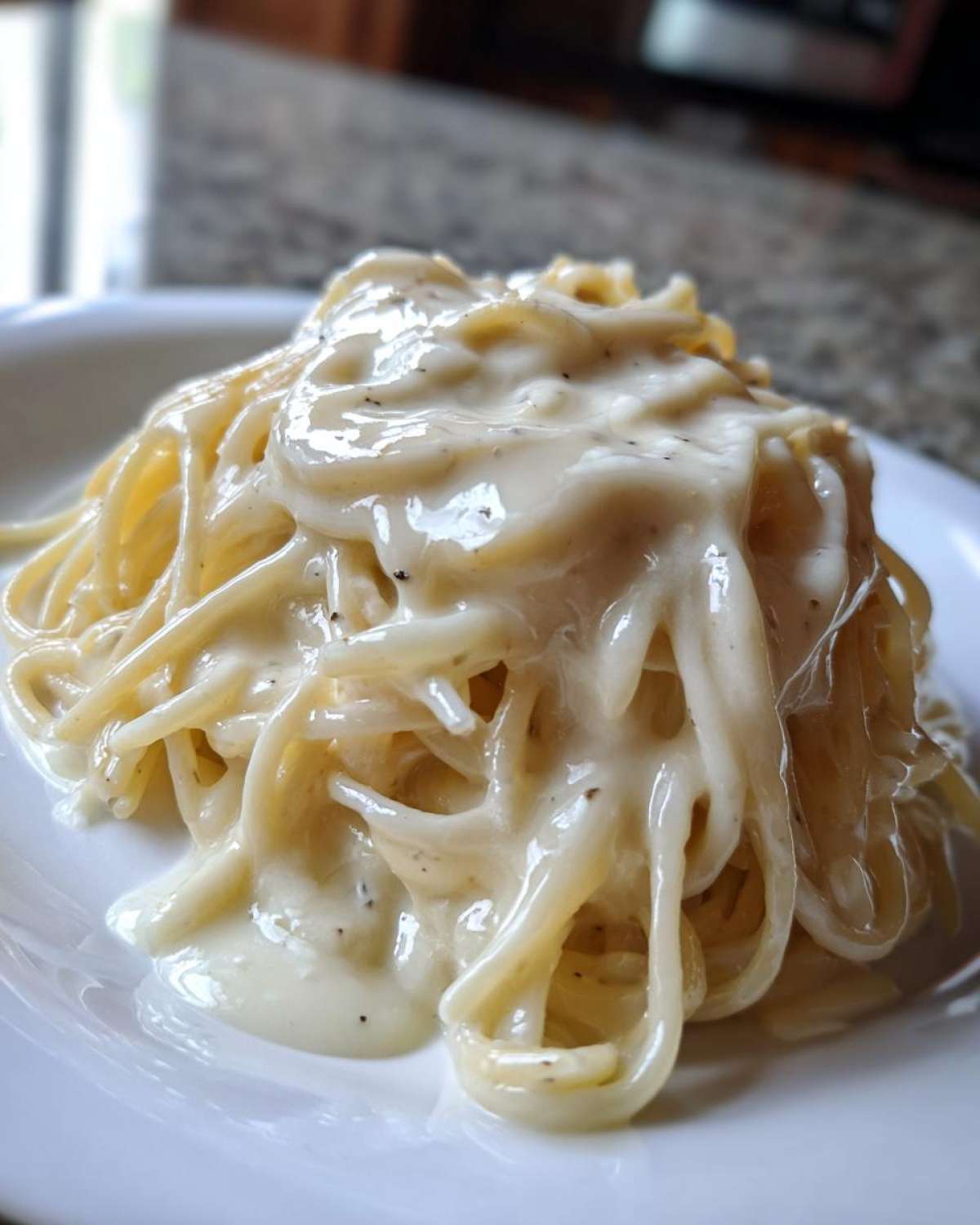 Close-up of spaghetti noodles generously coated in rich, creamy Olive Garden Alfredo Sauce with visible specks of black pepper.