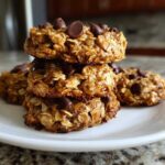 A stack of four homemade, chewy breakfast cookie oat bites topped with chocolate chips on a white plate.