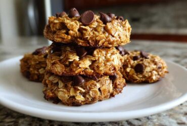 A stack of four homemade, chewy breakfast cookie oat bites topped with chocolate chips on a white plate.