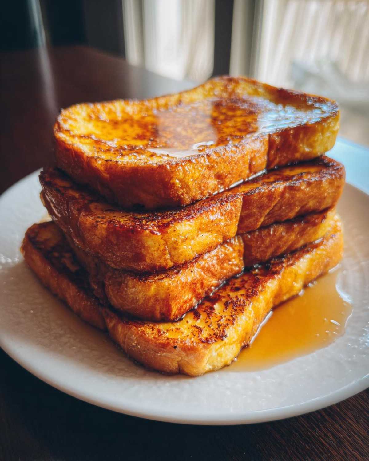 A tall stack of golden brown easy french toast slices drizzled generously with maple syrup on a white plate.