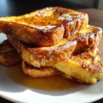 A tall stack of golden brown easy french toast slices drizzled with syrup on a white plate.
