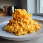 A close-up of a mound of creamy, orange cheesy rice with long, satisfying cheese pulls.