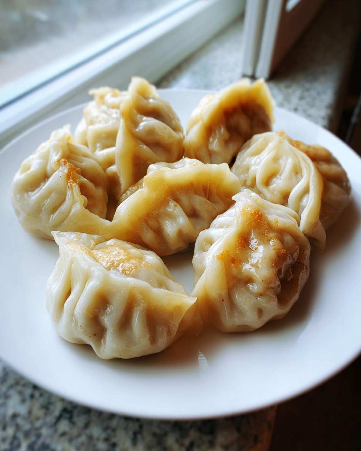 A white plate filled with several golden-brown Traditional Chinese Dumplings, lightly seared on the bottom.