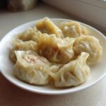 A white plate filled with several freshly steamed Traditional Chinese Dumplings, showing the savory meat filling.