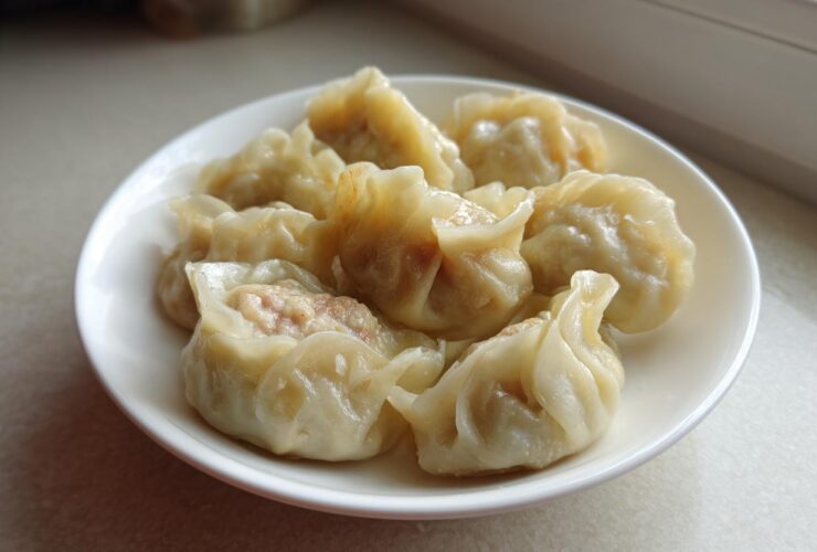 A white plate filled with several freshly steamed Traditional Chinese Dumplings, showing the savory meat filling.