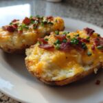 Two halves of twice-baked potatoes stuffed with creamy filling, melted cheddar cheese, bacon bits, and chives.