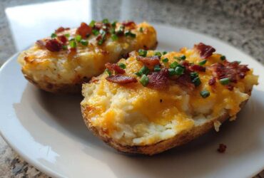 Two halves of twice-baked potatoes stuffed with creamy filling, melted cheddar cheese, bacon bits, and chives.