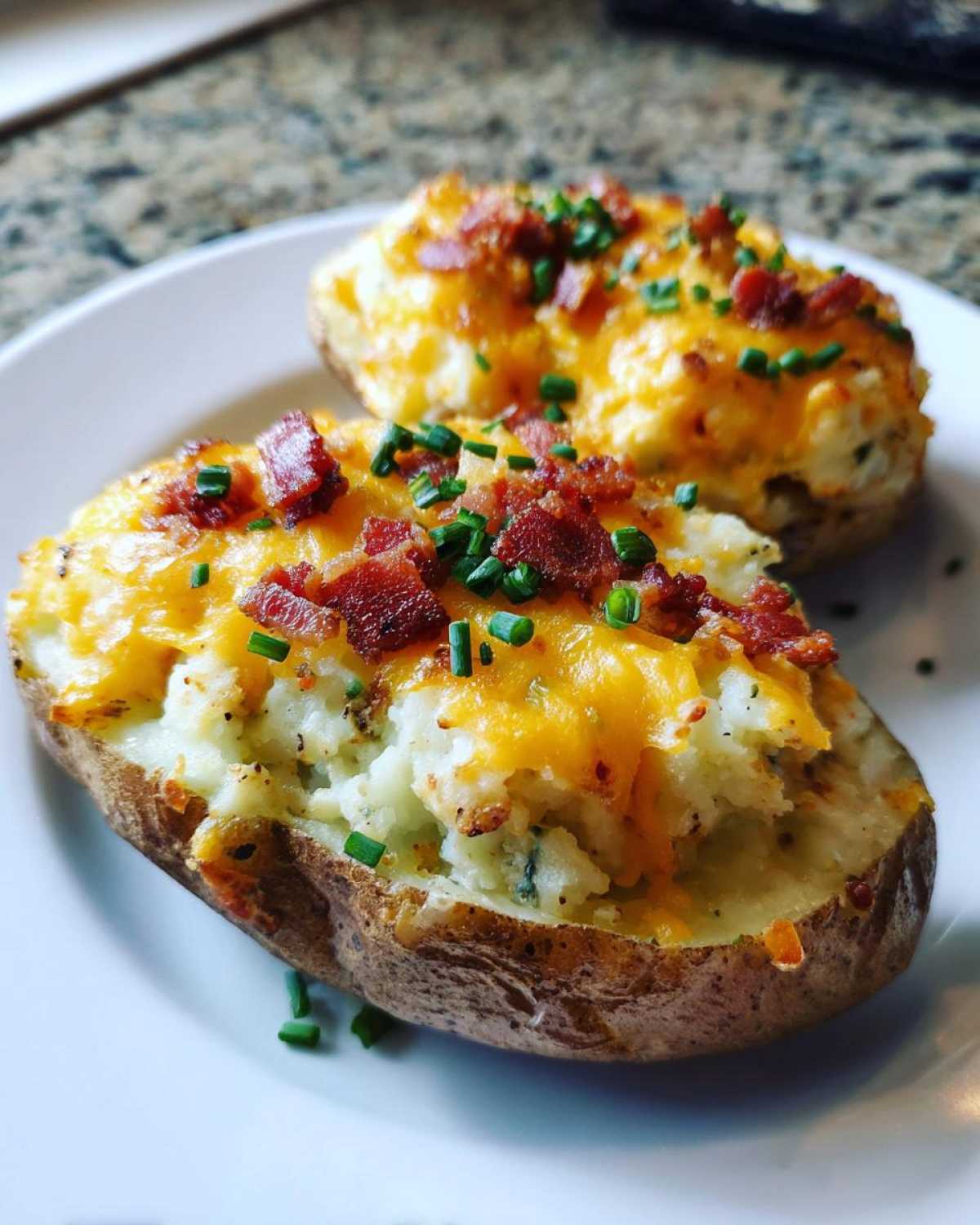 Two perfectly prepared twice-baked potatoes loaded with melted cheddar cheese, bacon bits, and fresh chives.