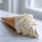 A waffle cone filled with a generous swirl of creamy, white vanilla buttercream frosting.