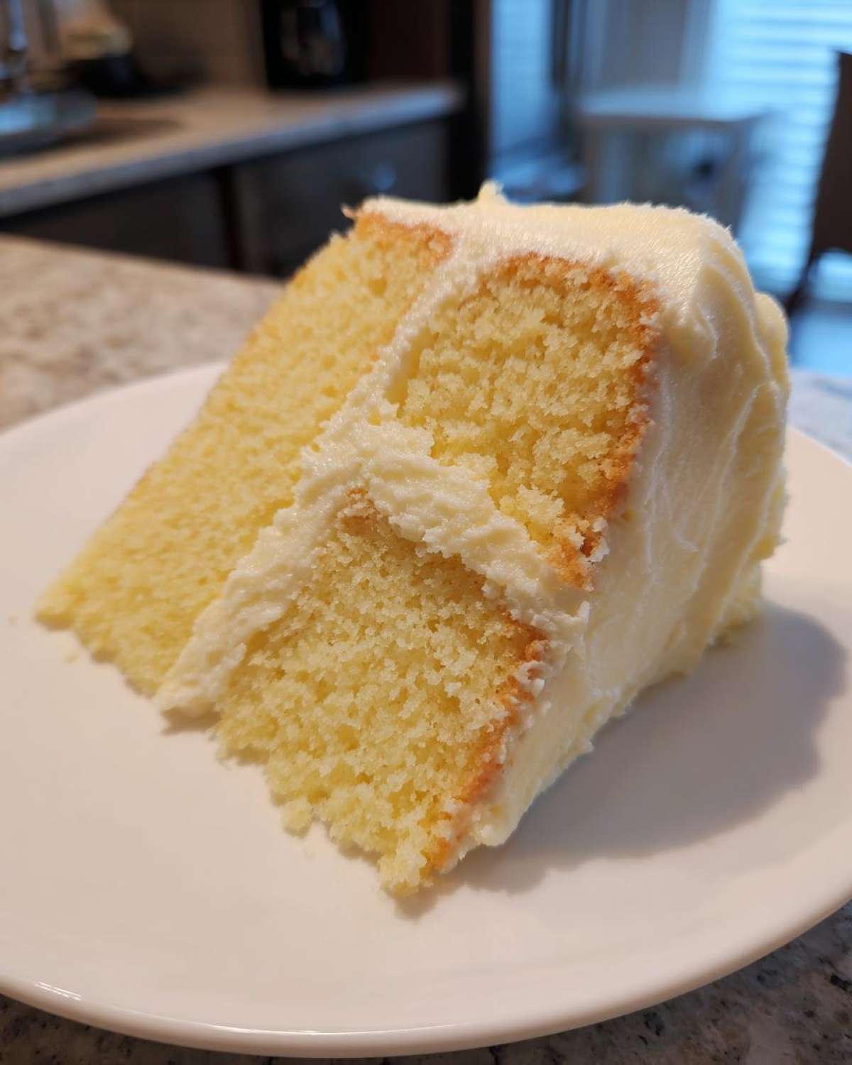 Close-up of a moist slice of yellow vanilla cake recipe layered and covered in thick white vanilla frosting.