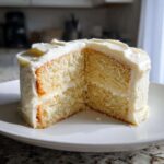 A thick slice of moist vanilla cake recipe cut in half, showing two layers and rich white buttercream frosting.