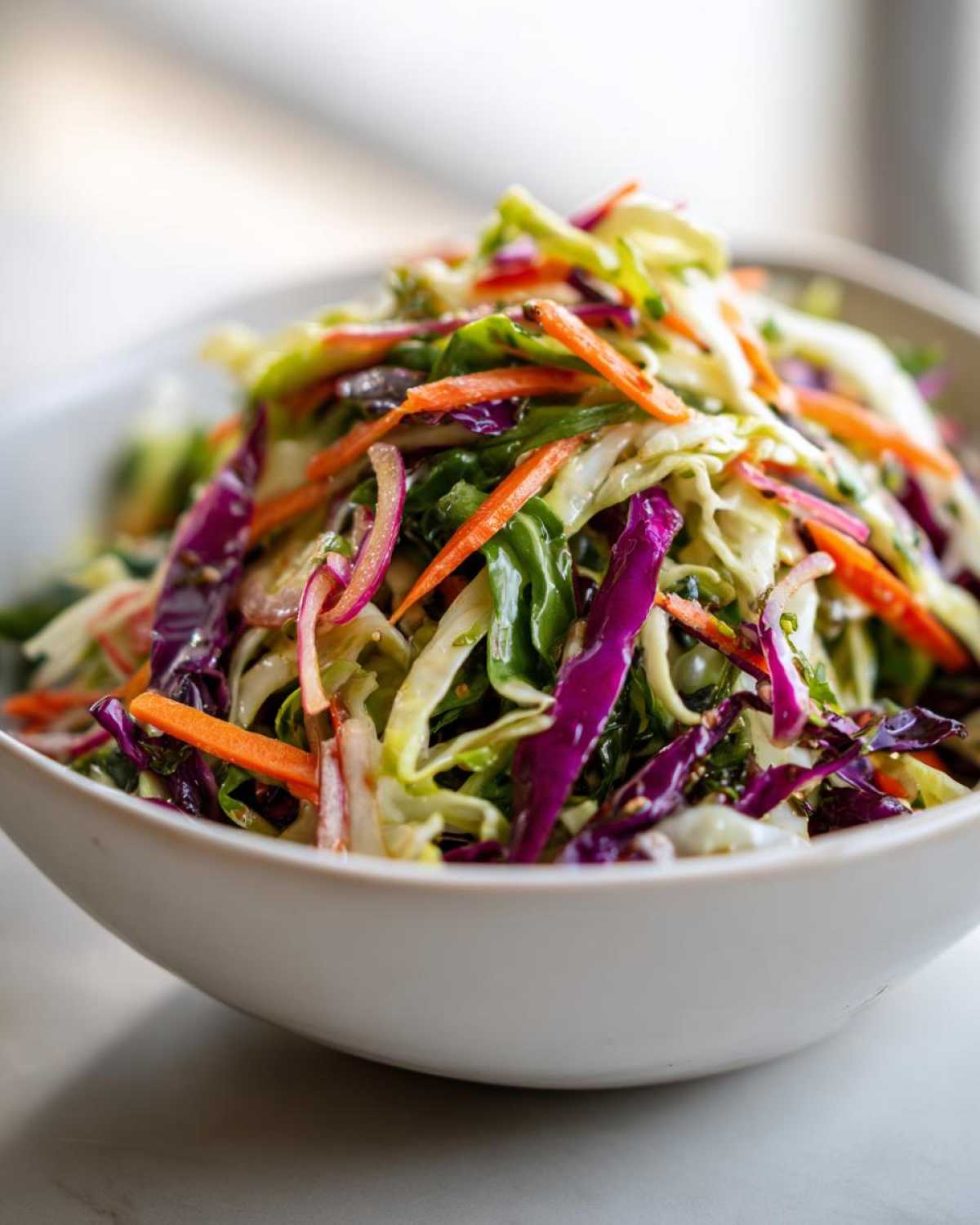 Close-up of a vibrant cabbage salad featuring shredded green and red cabbage, carrots, and onions in a white bowl.