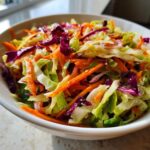 Close-up of a vibrant bowl filled with shredded green and purple cabbage and carrots in a fresh cabbage salad.