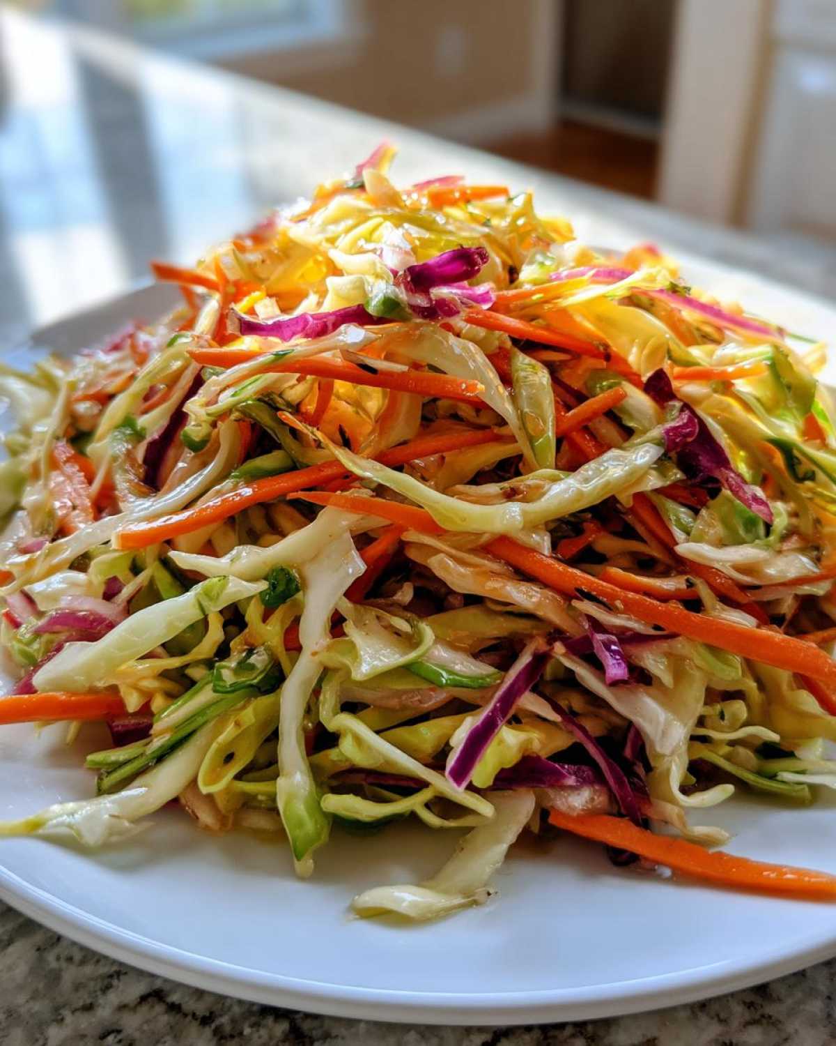 A close-up of a vibrant, freshly tossed cabbage salad featuring shredded green and purple cabbage and bright orange carrots.