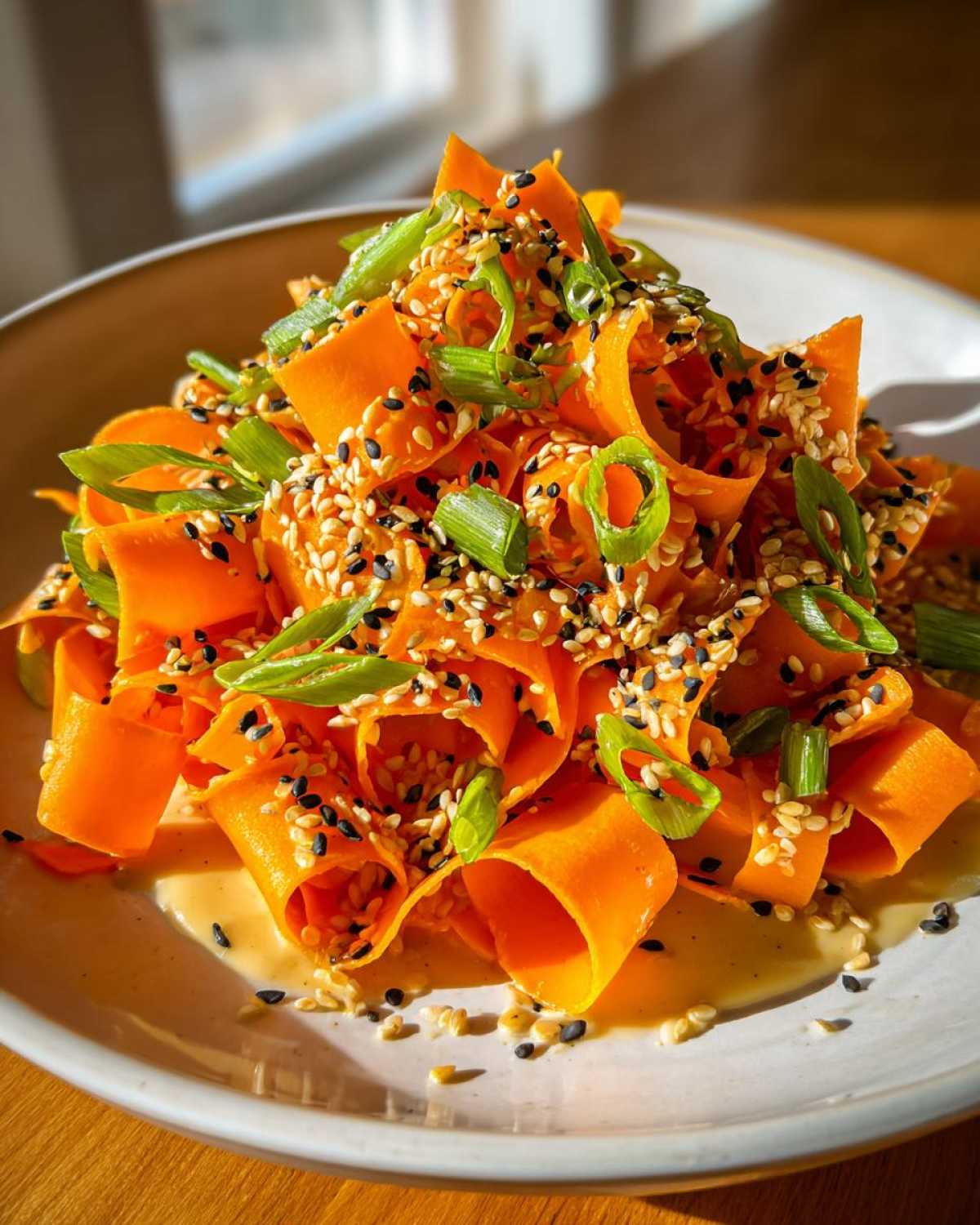 Close-up of a vibrant raw carrot salad made with shaved carrot ribbons, topped generously with sesame seeds and green onions.