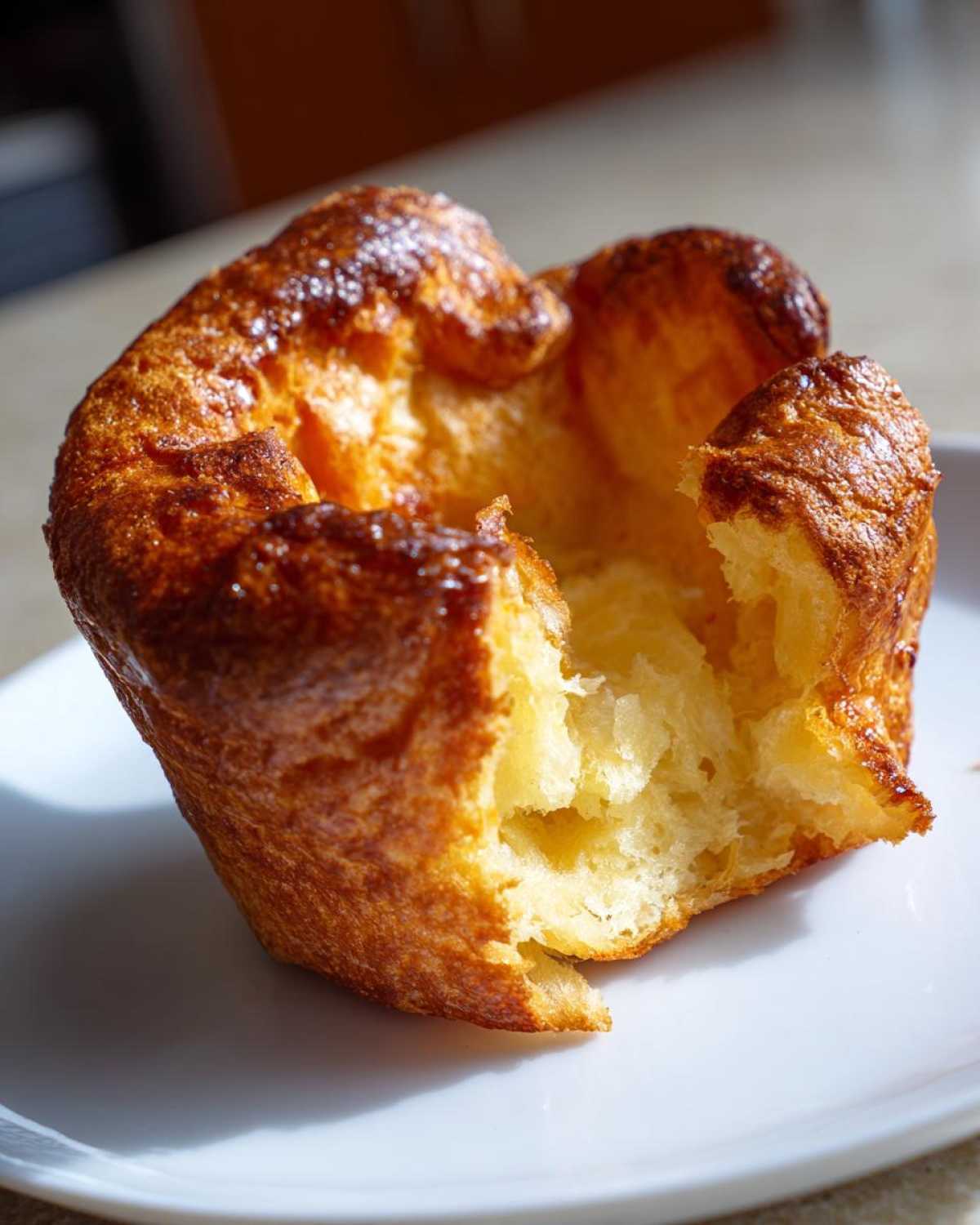 Close-up of a golden brown, fully risen Yorkshire pudding with a hollow center, sitting on a white plate.
