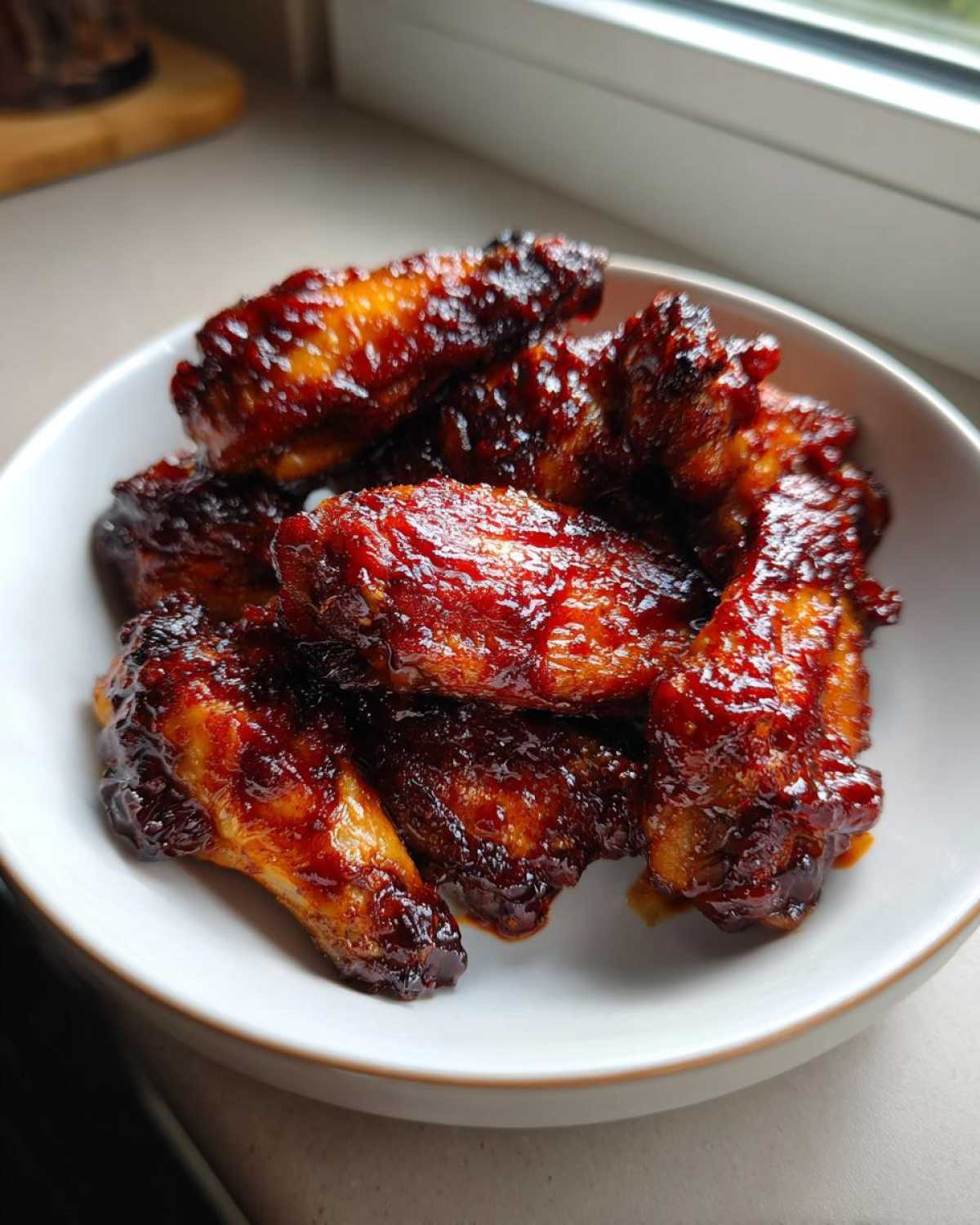 A white bowl filled with glossy, dark red Air Fryer BBQ Chicken Wings, perfectly glazed and cooked.