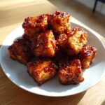 Close-up of golden, crispy Air Fryer Crispy Tofu with Sweet Chili Glaze piled on a white plate.