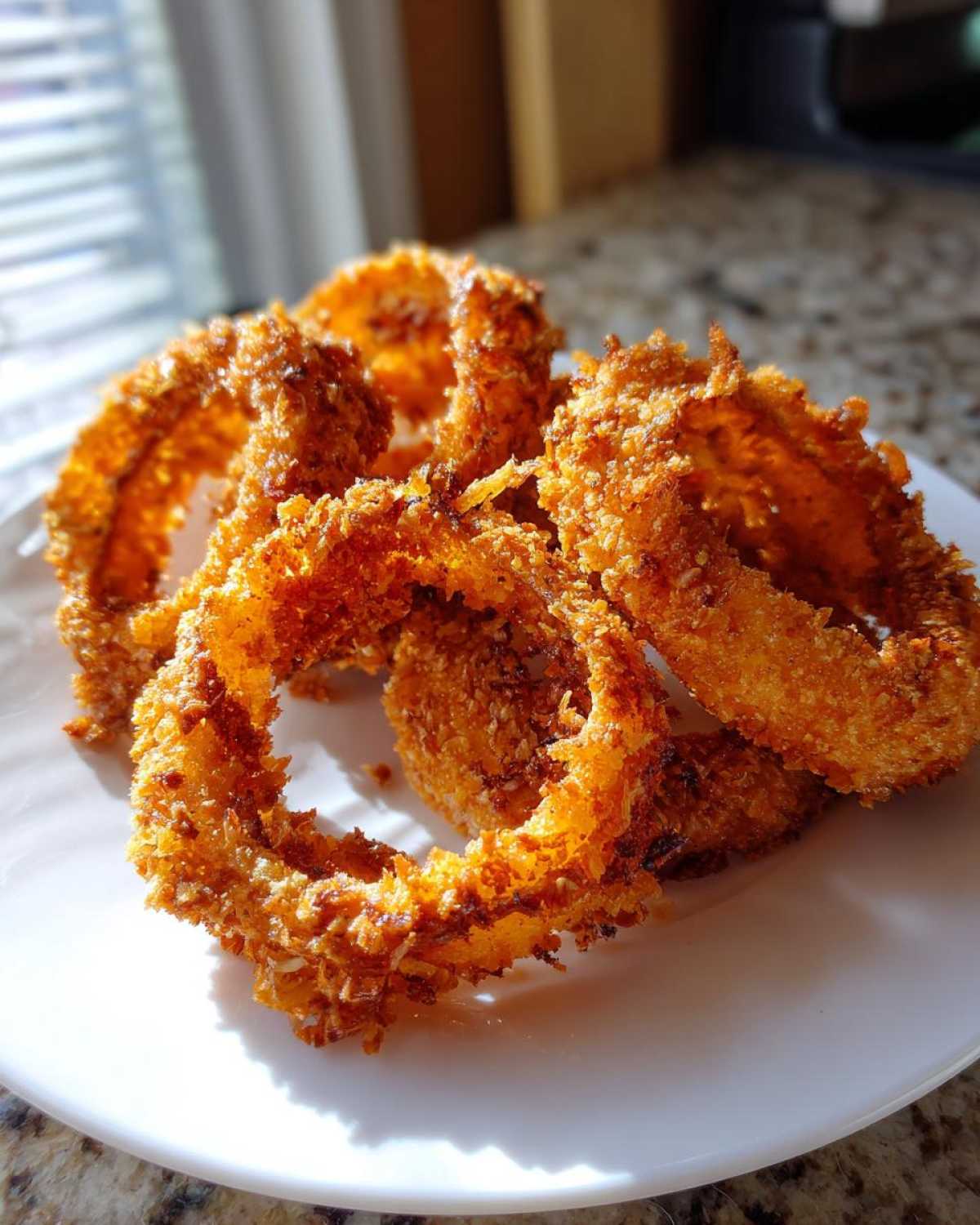A close-up of several golden brown, crispy Air Fryer Onion Rings piled on a white plate.