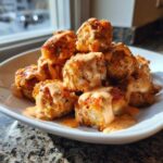 A pile of crispy Air Fryer Salmon Bites generously drizzled with creamy Bang Bang Sauce on a white plate.