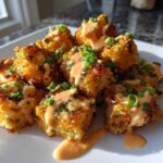 A pile of crispy, golden Air Fryer Salmon Bites drizzled with creamy Bang Bang Sauce and topped with chives.