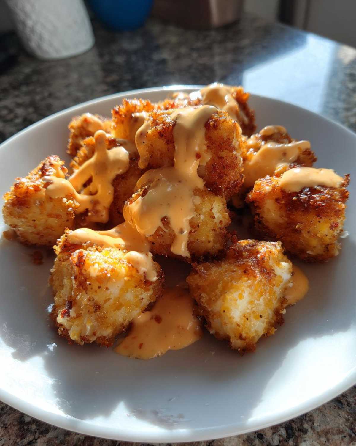 Golden brown, crispy Air Fryer Salmon Bites drizzled generously with creamy Bang Bang Sauce on a white plate.