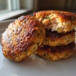 A stack of three golden-brown Air Fryer Salmon Patties, with the top one broken open showing the flaky pink salmon interior.