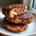 Three golden-brown Air Fryer Salmon Patties stacked, with the top one broken open to show flaky salmon inside.