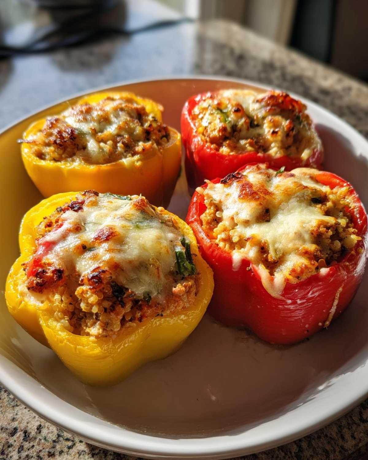 Four colorful Air Fryer Stuffed Bell Peppers (two red, two yellow) topped with bubbly, melted cheese.