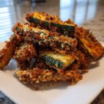 A pile of golden brown, crispy Air Fryer Zucchini Fries with Parmesan stacked on a white plate.