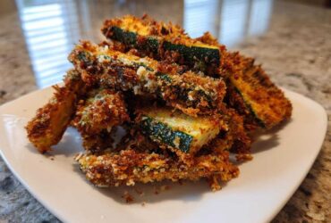 A pile of golden brown, crispy Air Fryer Zucchini Fries with Parmesan stacked on a white plate.