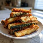 A stack of crispy, golden brown Air Fryer Zucchini Fries with Parmesan piled on a white plate.
