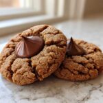 Two classic Peanut Butter Blossom Cookies with a melted chocolate kiss center resting on a light countertop.