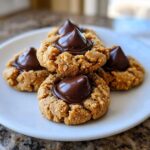A stack of four delicious Peanut Butter Blossom Cookies topped with melted chocolate kisses on a white plate.