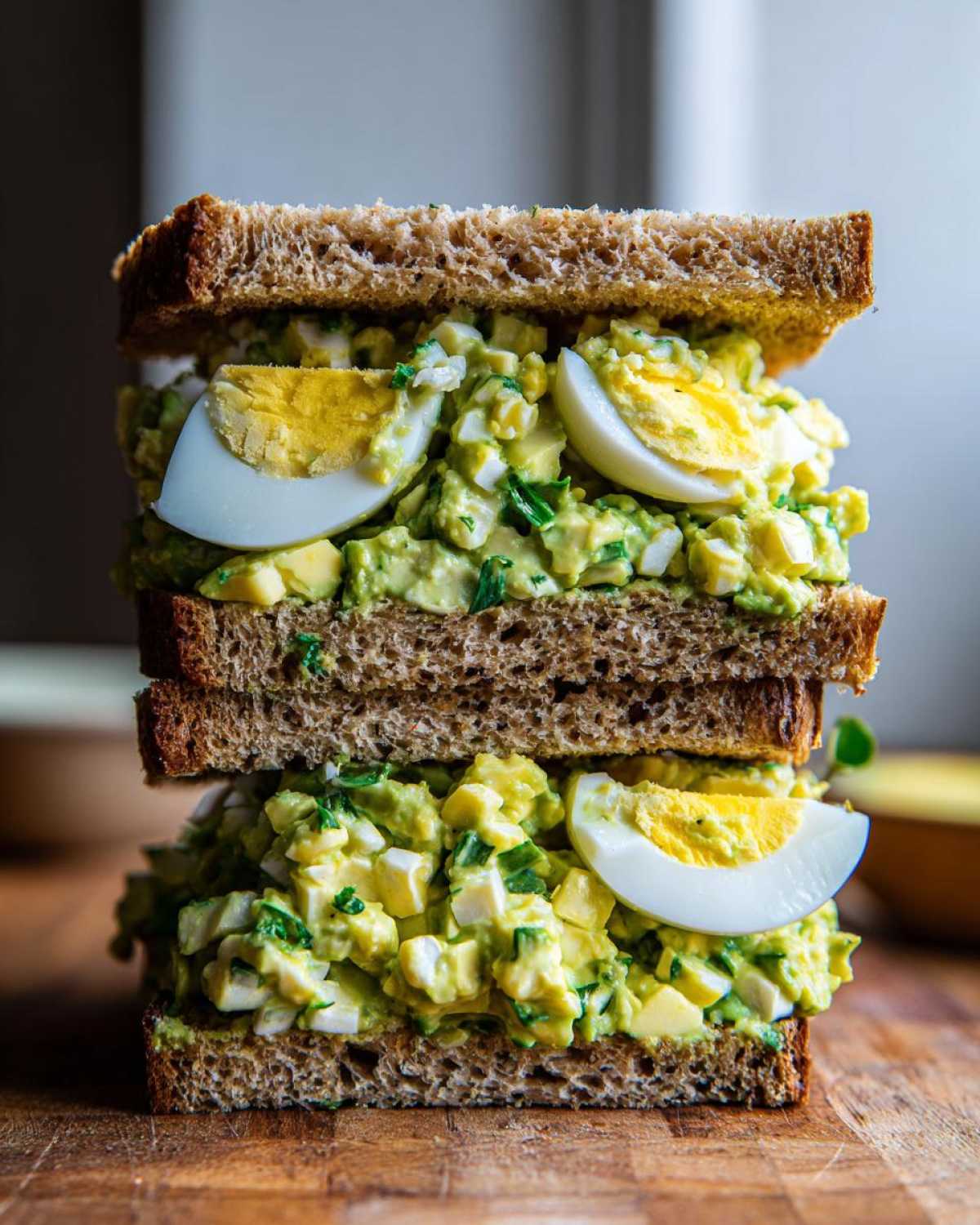 A tall, stacked Avocado Egg Salad Sandwich made with whole wheat bread and visible slices of hard-boiled egg.