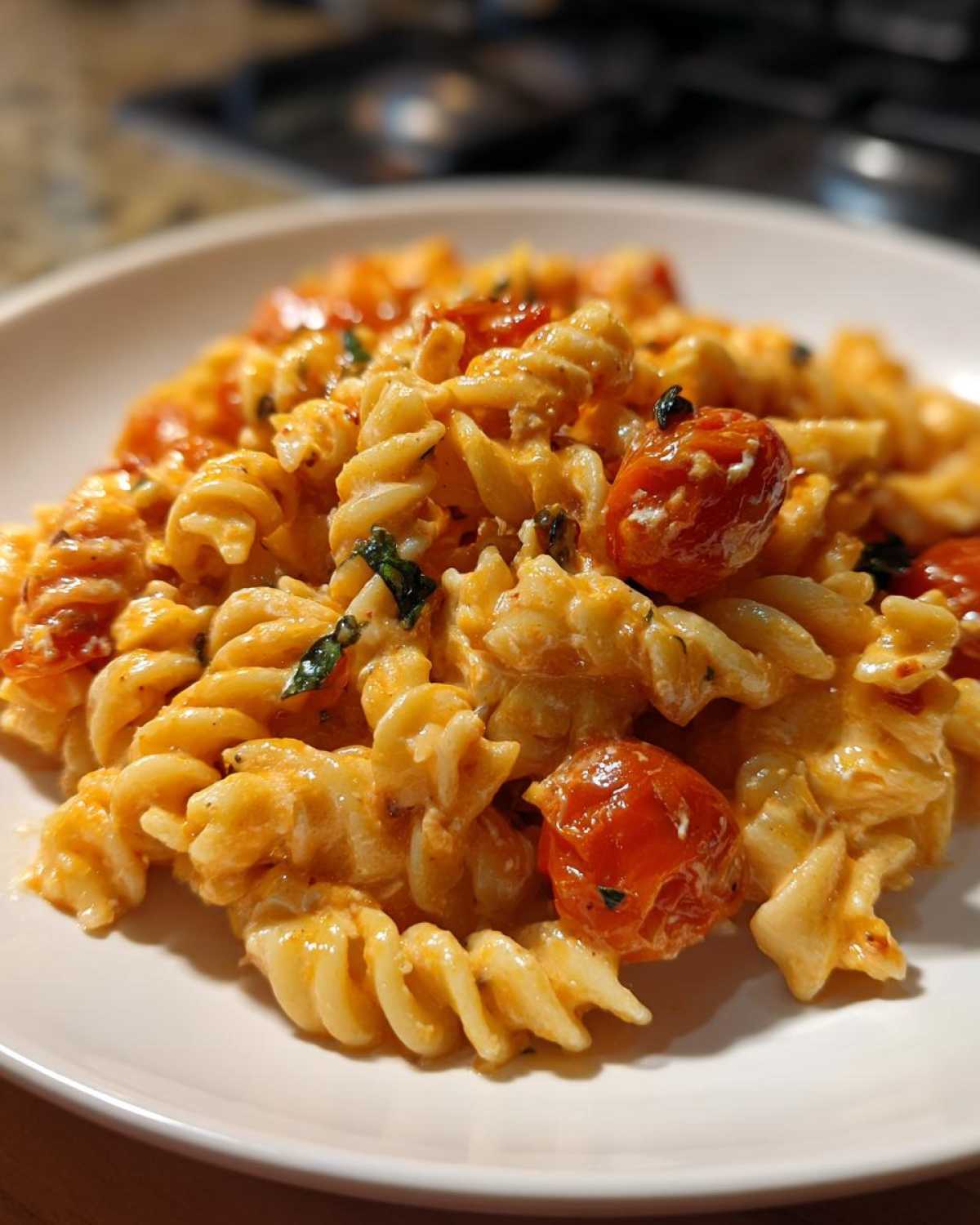 Close-up of Baked Feta Pasta with cherry tomatoes and basil served on a white plate.