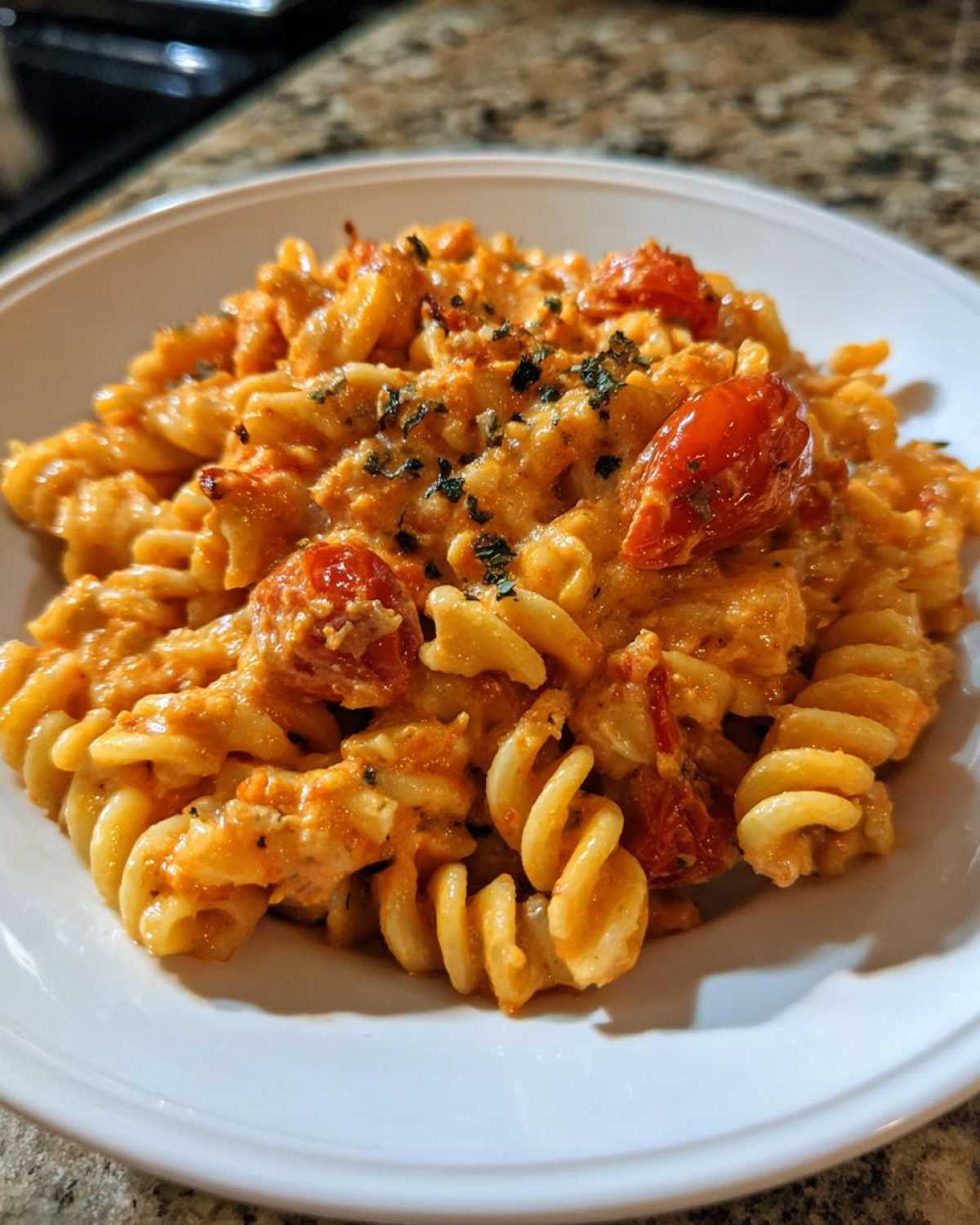 A close-up of creamy Baked Feta Pasta with Cherry Tomatoes mixed with fusilli pasta, garnished with herbs.