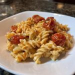 A close-up of creamy Baked Feta Pasta with spiral fusilli noodles and roasted cherry tomatoes in a white bowl.