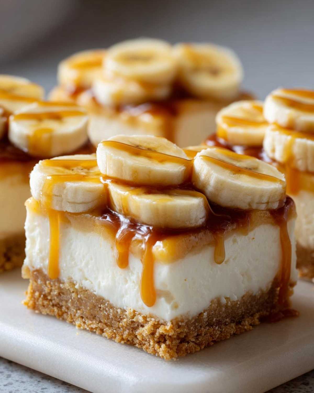 A decadent square of Banana Pudding Cheesecake Bars featuring a thick graham cracker crust, creamy filling, and topped with banana slices and caramel drizzle.