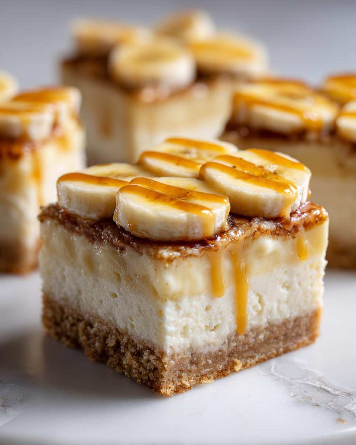 A decadent square of Banana Pudding Cheesecake Bars topped with fresh banana slices and caramel drizzle.