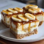 Three decadent slices of Banana Pudding Cheesecake Bars topped with banana slices and caramel drizzle.